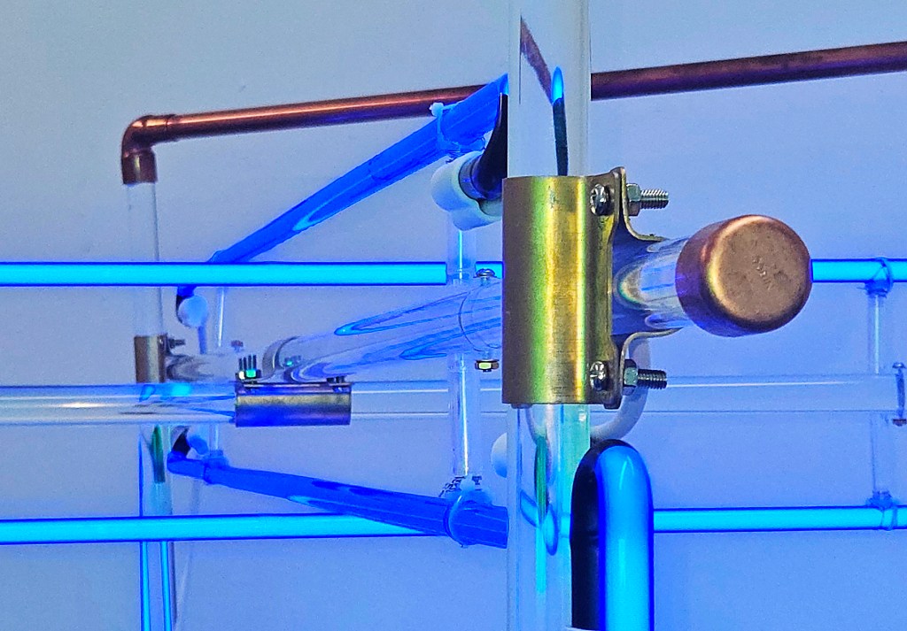 The Chiasm, is a Cobalt blue neon light and mirror sculpture installation with the semblance of a deconstructed manifestation of Constructivist Taitlin’s Tower. Senstad utilizes utilitarian, readymade materials, construction scaffolding aesthetics, and copper plumbing parts, reflecting the sacred in the ordinary. The installation acts as a portal within a space.